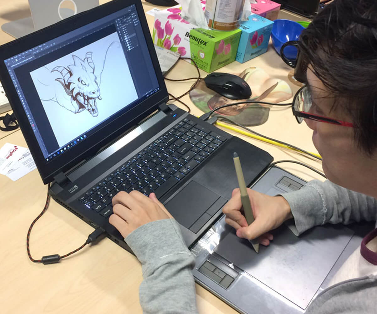 Alumnus Desmond Wong works on a dragon illustration using a laptop computer and tablet