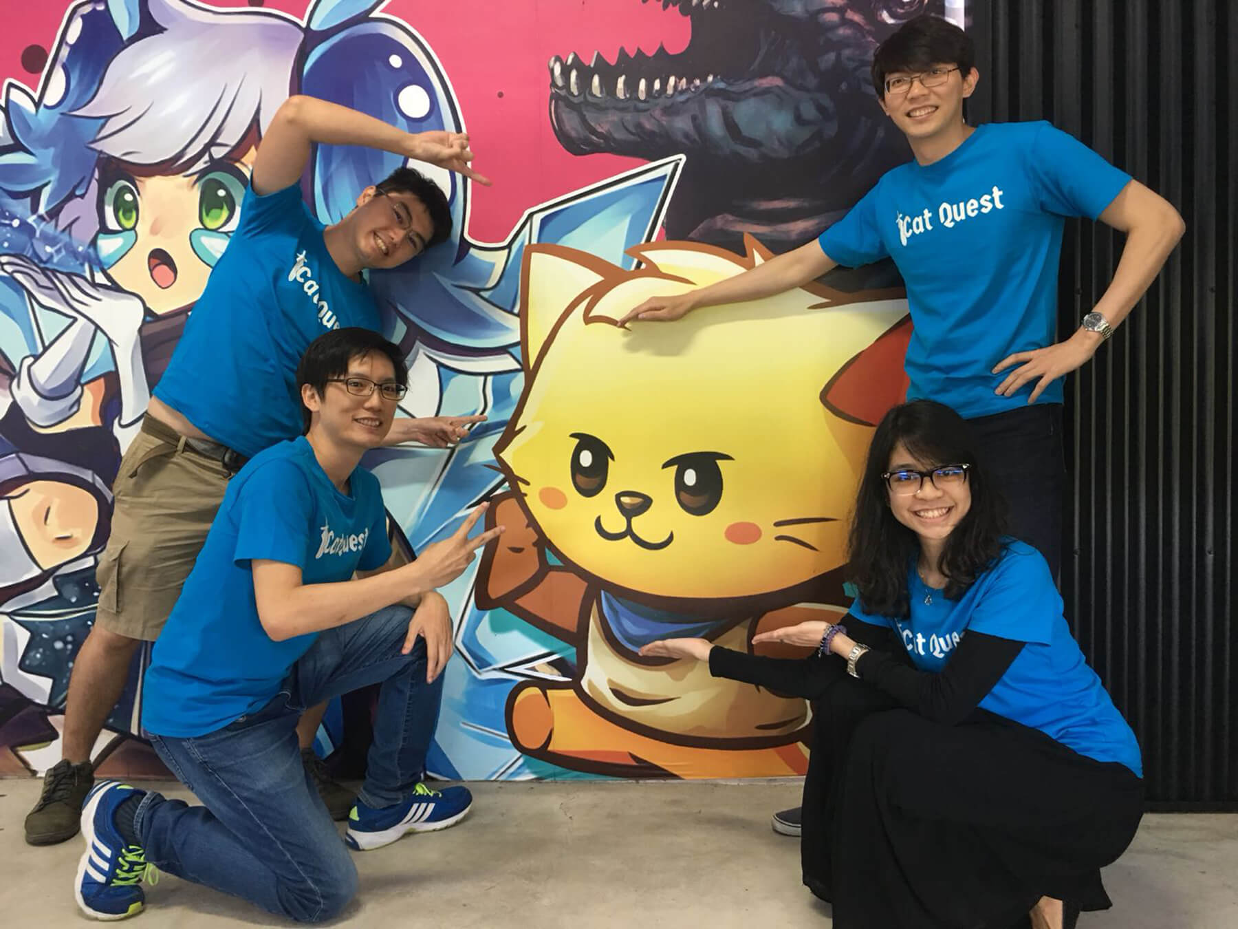 Four Gentlebros team members wearing Cat Quest T-shirts pose in front of a Cat Quest backdrop.