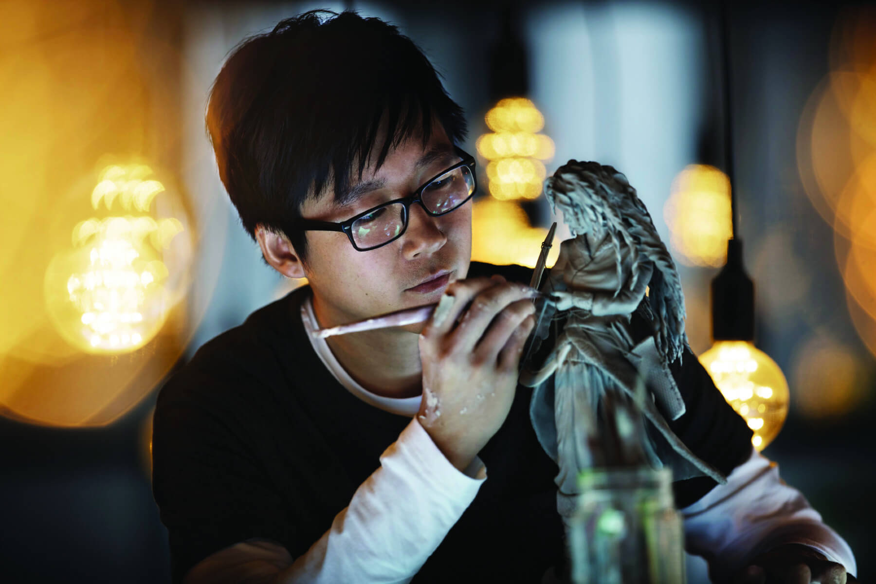Male student carefully sculpting a detailed female clay statue