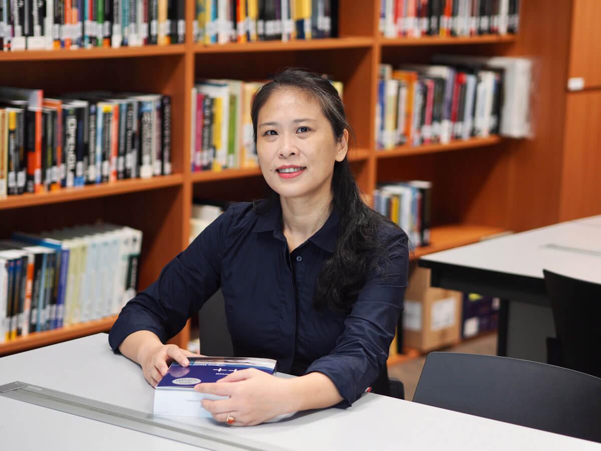 Photo of DigiPen Singapore staff Liu Fang sitting at a desk in a libray