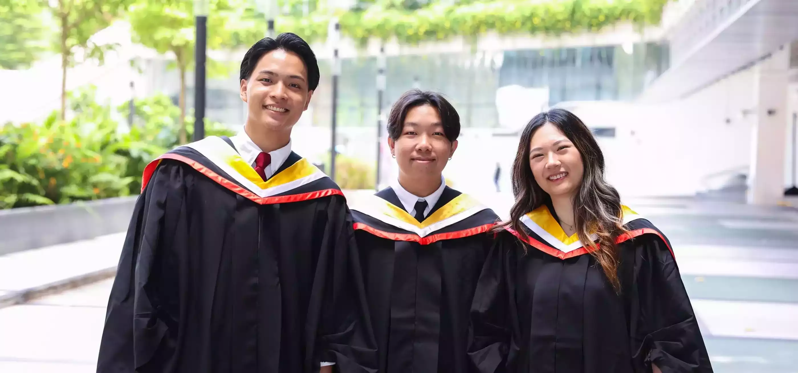 Three alumni pose in their commencement robes.