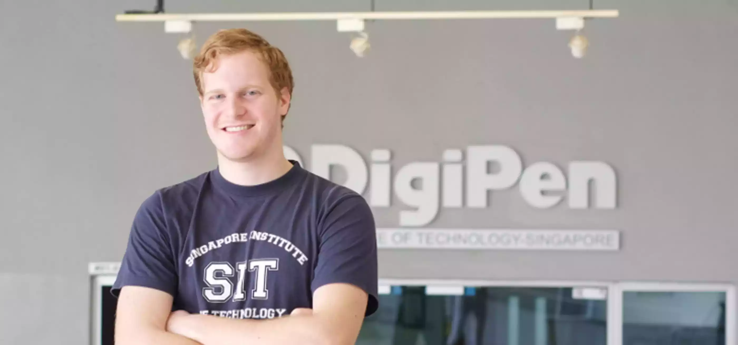 RTIS student Alan Miller poses for a photo arms crossed in front of a building. DigiPen logo is on the building behind him.