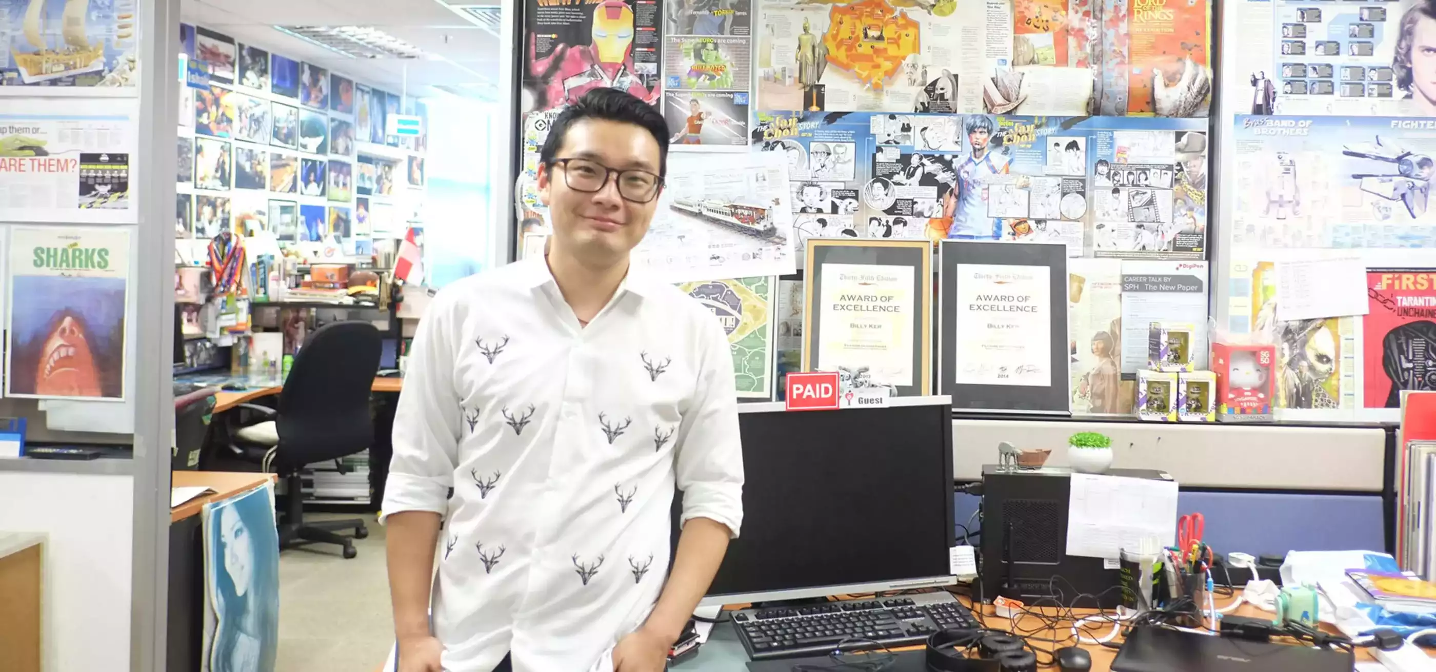 DigiPen graduate Billy Ker stands in an office with walls lined with various colorful printouts of infographics