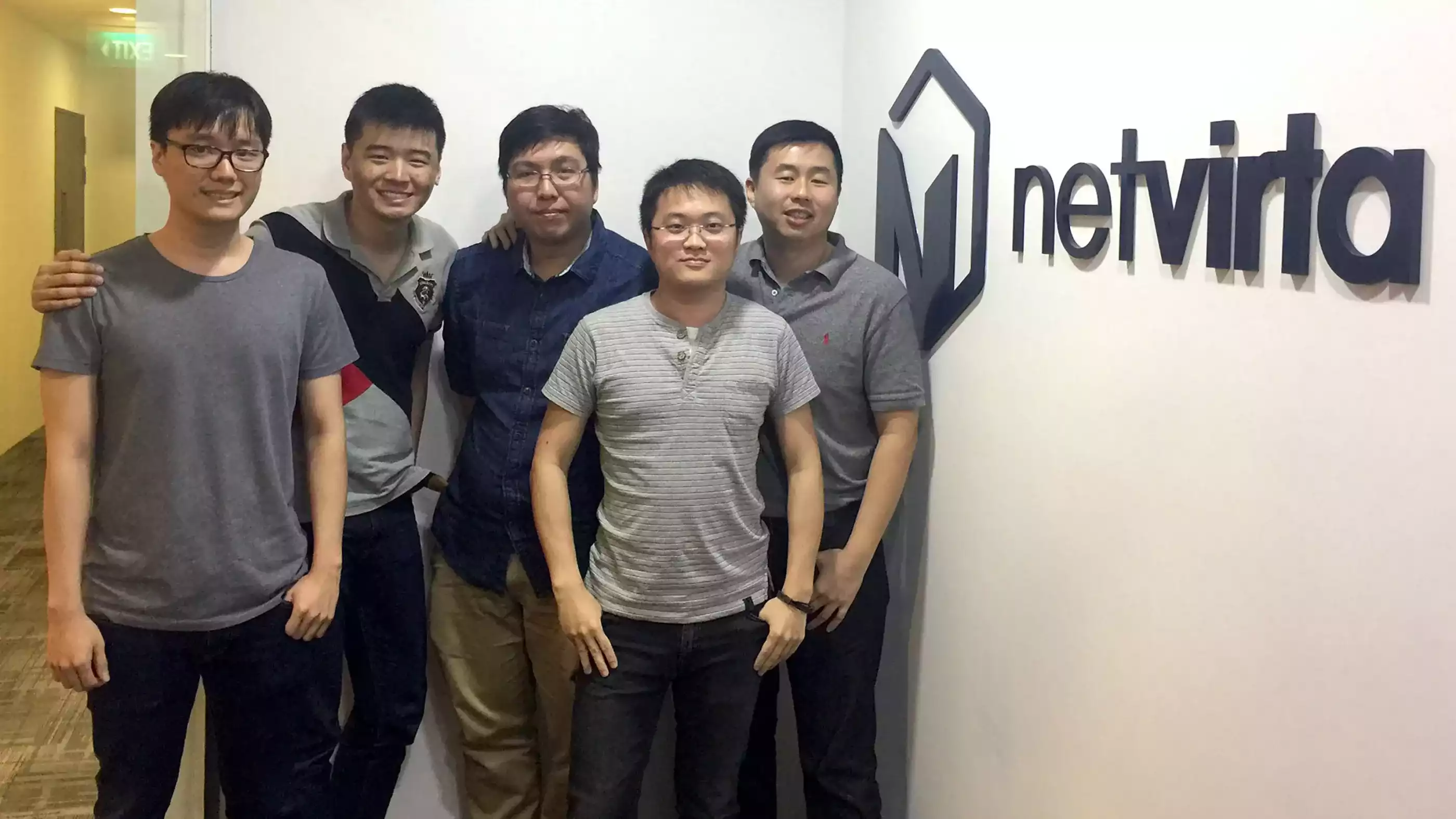 A group of DigiPen Singapore alumni pose next to the logo of Boston-based startup company NetVirta