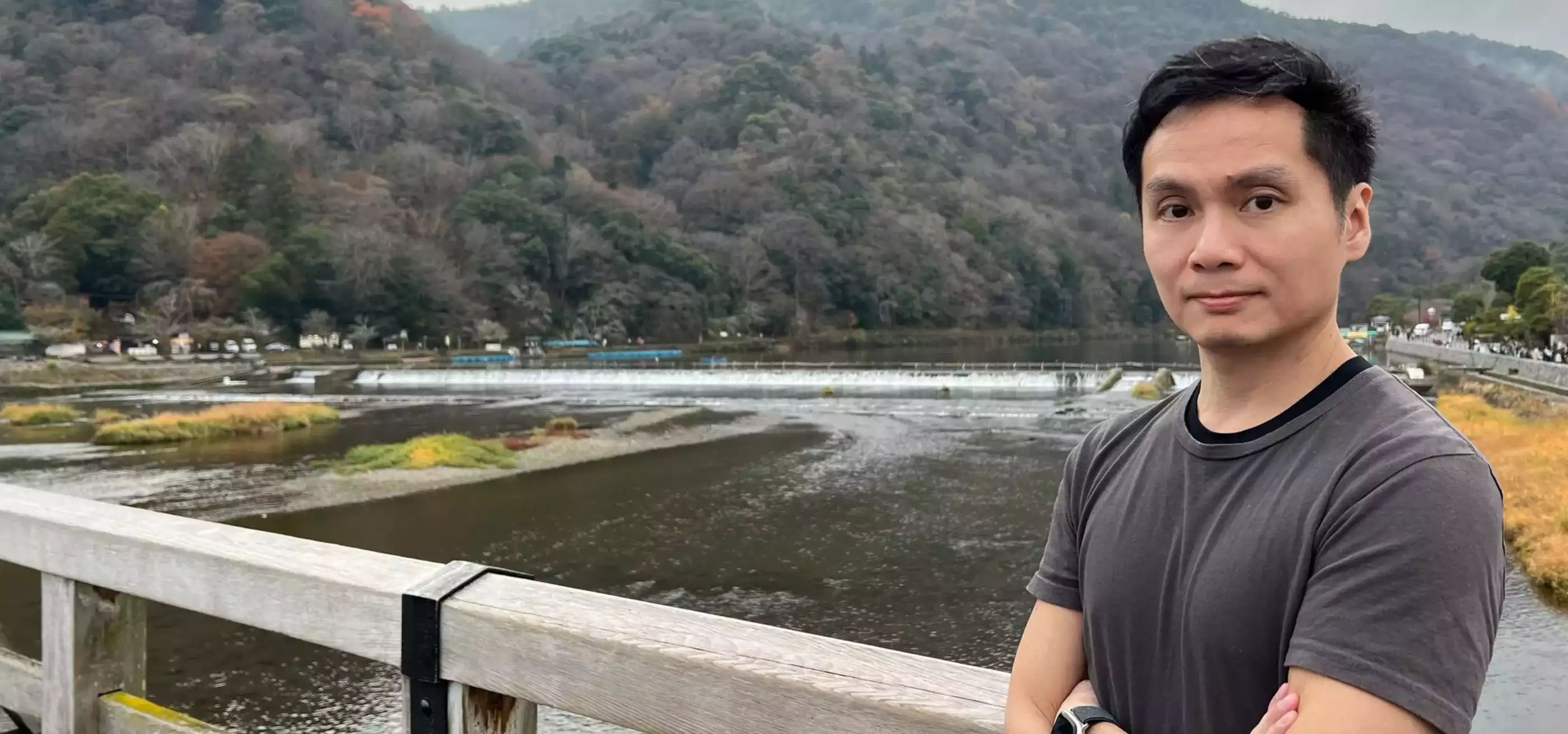 Asian man standing with his arms crossed against a scenic background of a mountain and lake