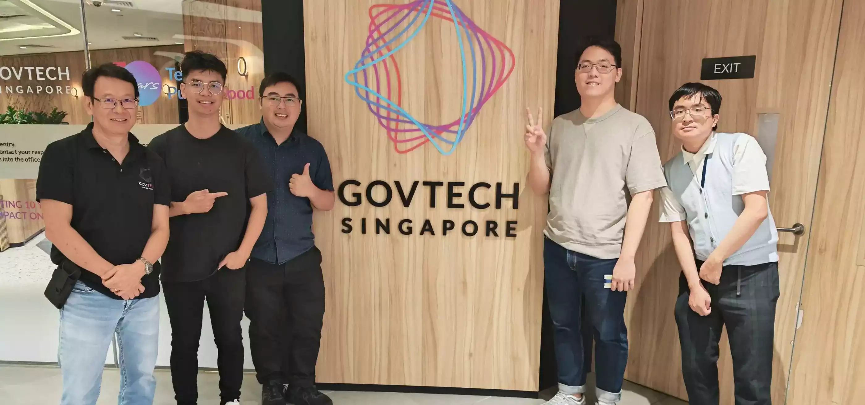 Four men stand around a logo in a building.
