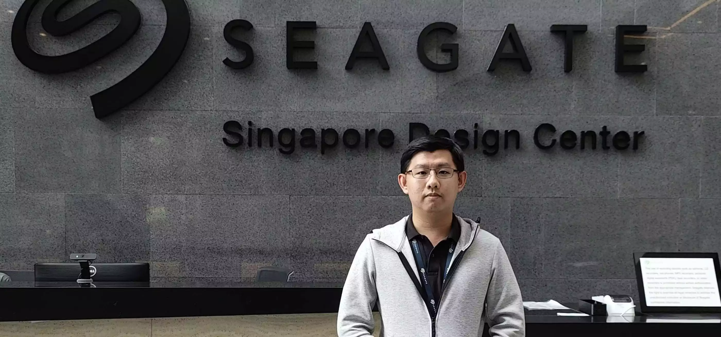DigiPen Graduate Toh Yu Xing stands in a building's lobby with the SEAGATE logo behind him