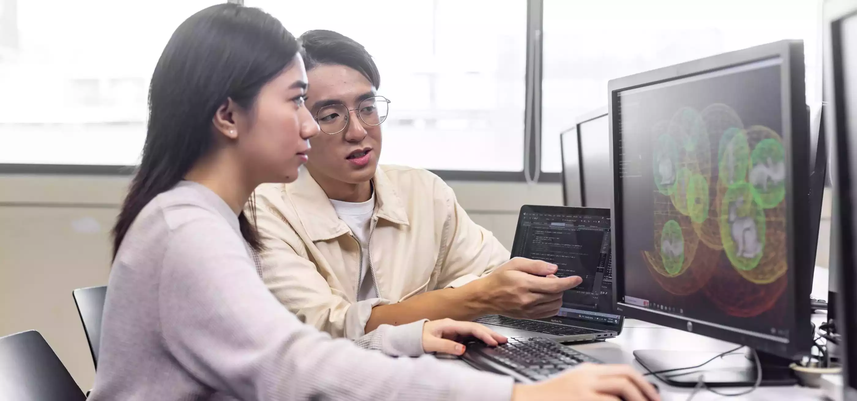 A professor sits next to a student in front of a computer.