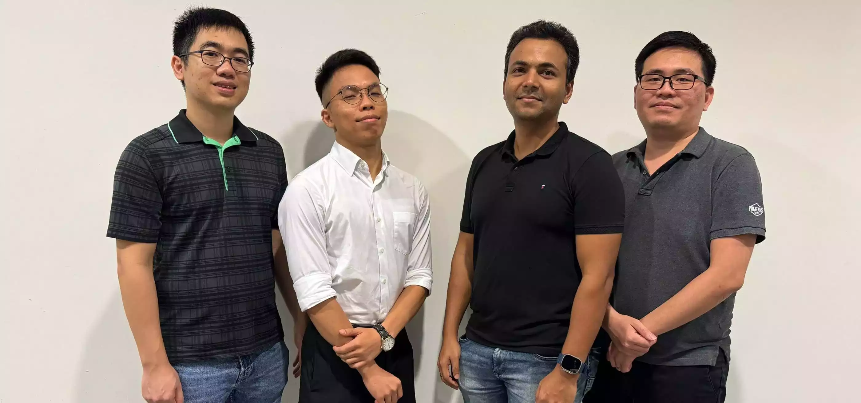 Four male students standing in front of a wall.
