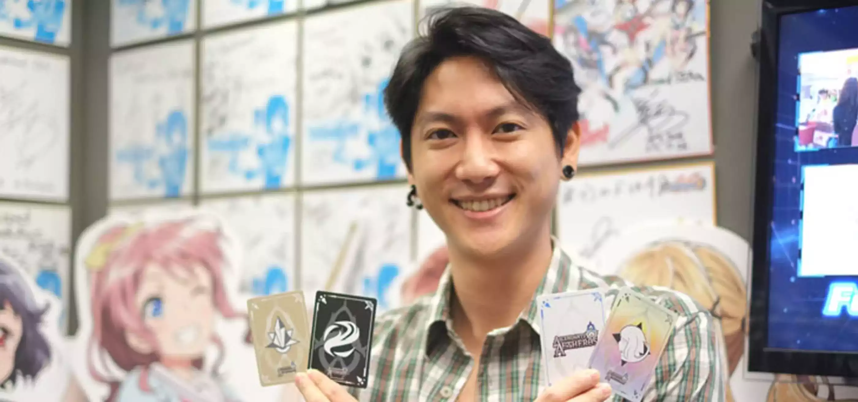 RTIS graduate Rudy Ng poses holding four cards from the card game Ascendants of Aetheros